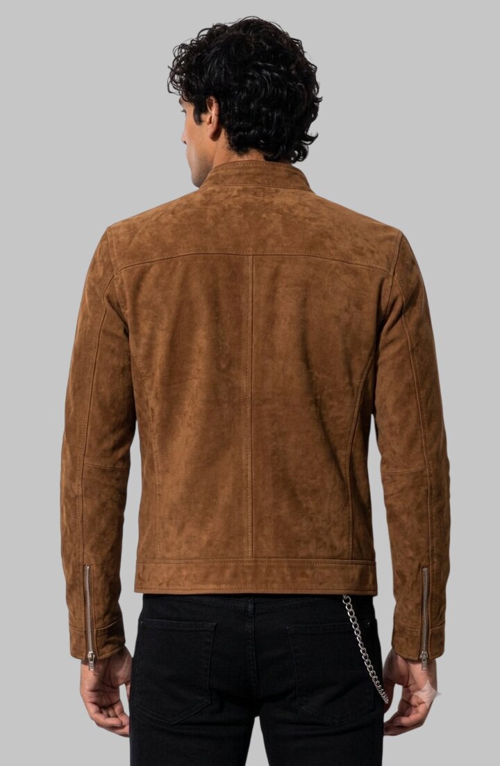 A man viewed from the back wearing a brown suede jacket and black pants against a solid gray studio background.