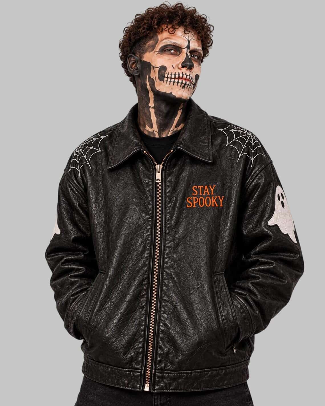 A person wearing a black leather jacket with Halloween graphics, including 'STAY SPOOKY' text on the chest, spiderwebs on the shoulders, a white ghost patch on the sleeve, and a skull face design in black and white makeup.