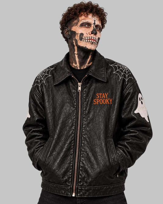 A person wearing a black leather jacket with Halloween graphics, including 'STAY SPOOKY' text on the chest, spiderwebs on the shoulders, a white ghost patch on the sleeve, and a skull face design in black and white makeup.