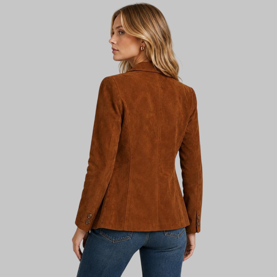 A woman shown from the back wearing a brown suede blazer and blue jeans against a solid gray studio background.