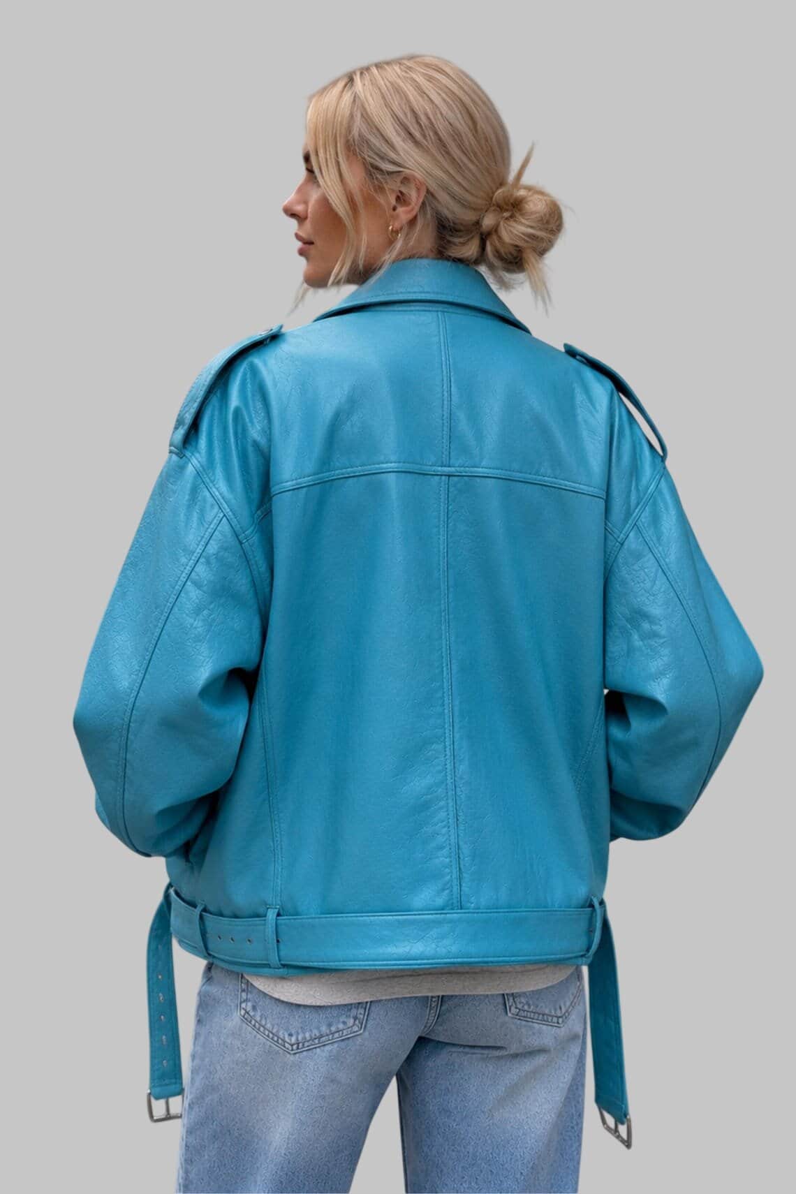 A woman shown from the back wearing a bright turquoise blue leather jacket with a belted waist and shoulder epaulets, paired with light-wash blue jeans, against a solid gray studio background.